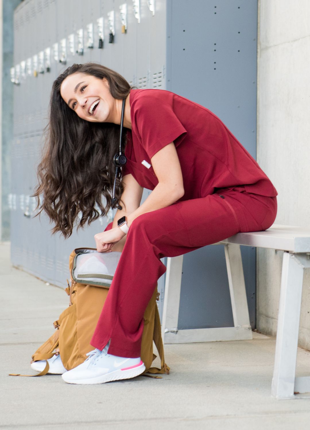 Women's burgundy red scrubs seated on bench.
