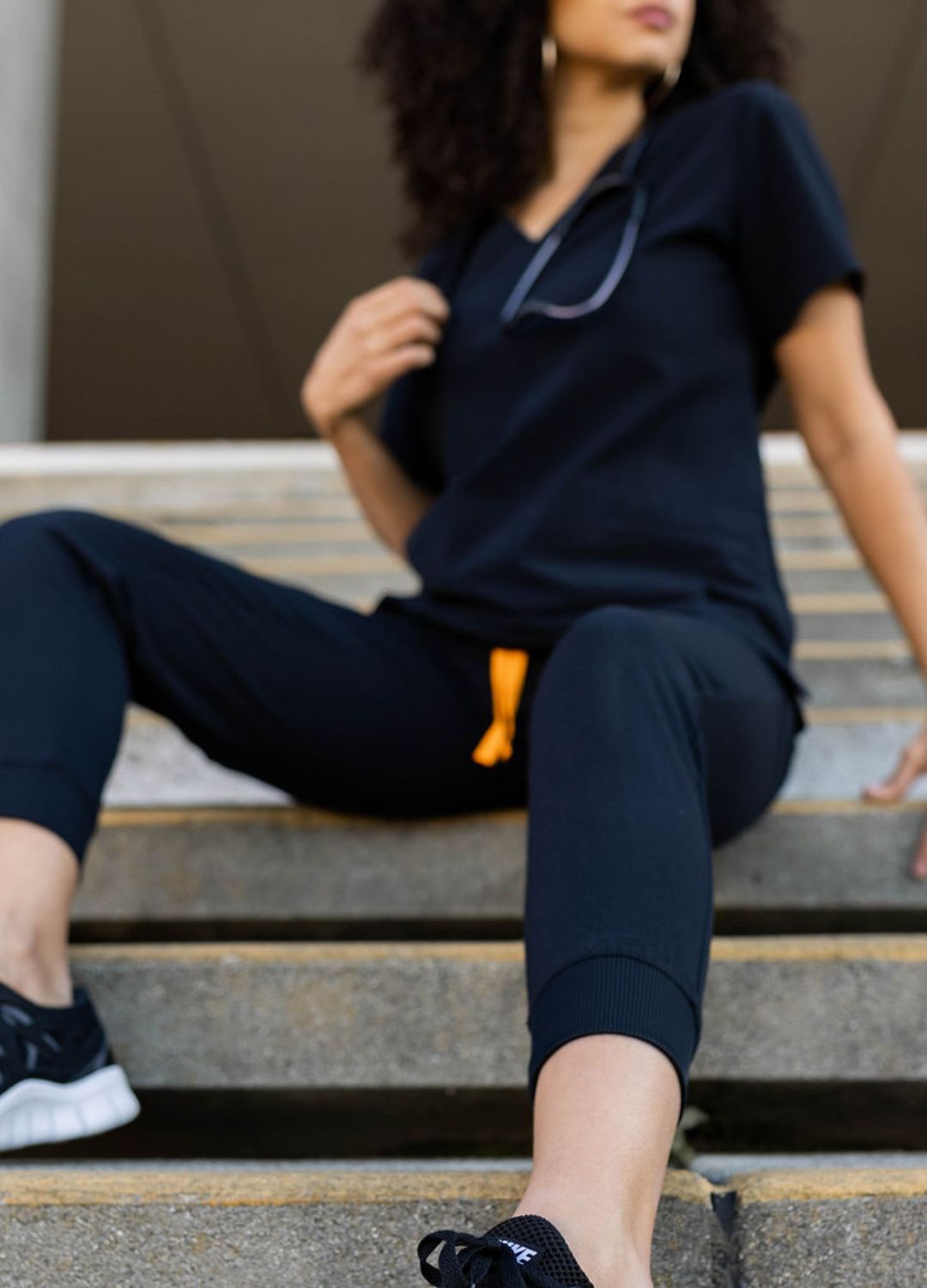 Poppy black jogger scrubs seated on stairs.