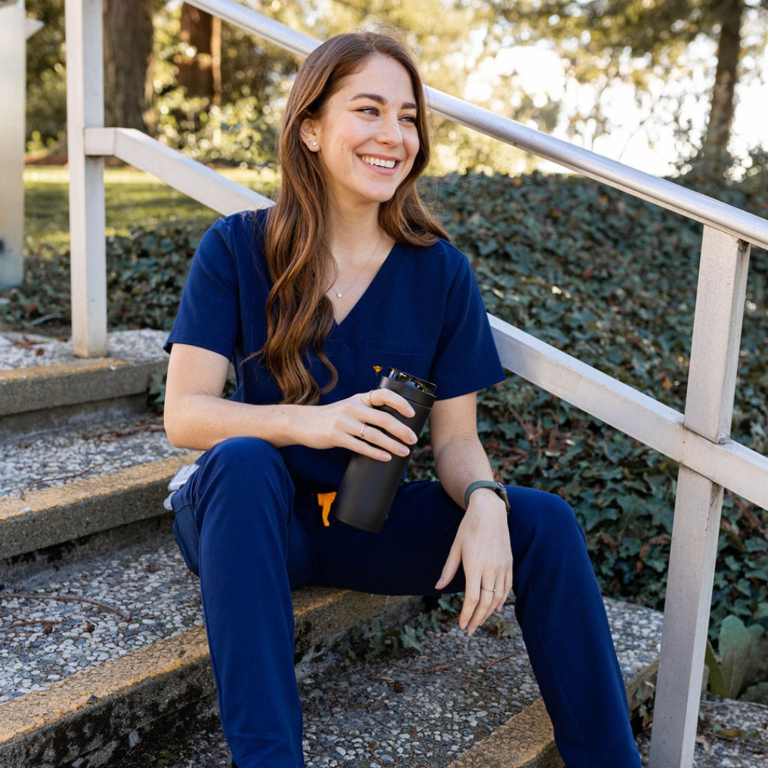 Full body picture of nurse sitting in navy scrubs.