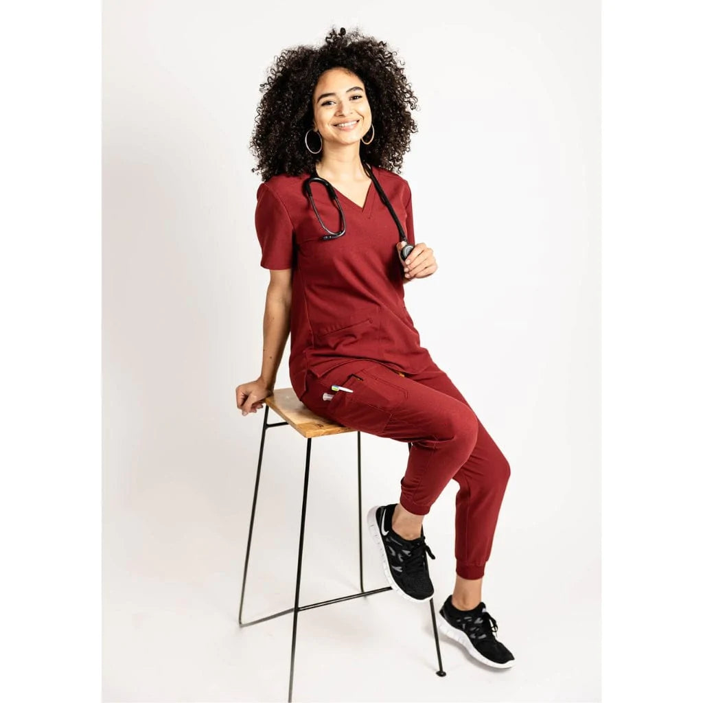 Seated full body picture of the the Hatton jogger scrub pants in burgundy.