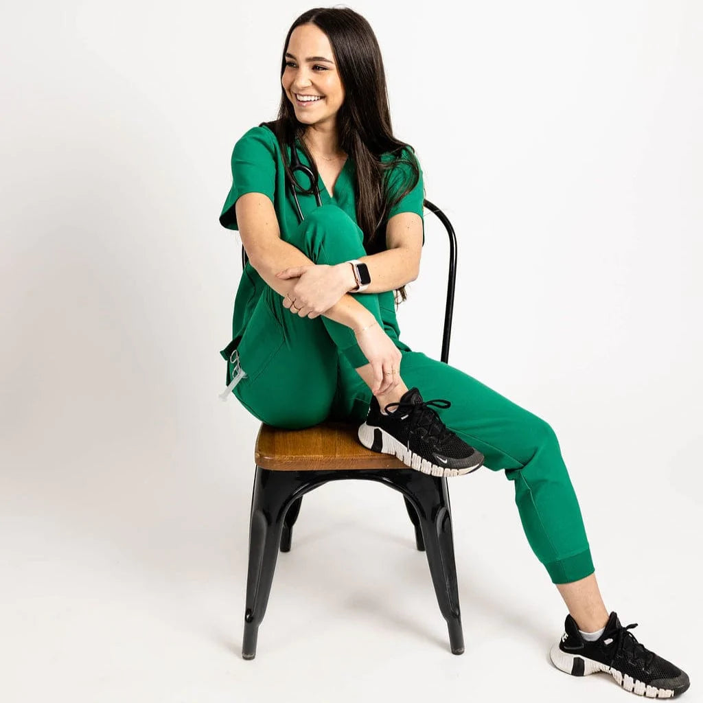 Full body seated picture of the the Hatton jogger scrub pants in hunter green.