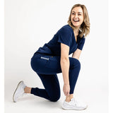 Kneeling full body picture of the the Hatton jogger scrub pants in navy blue.