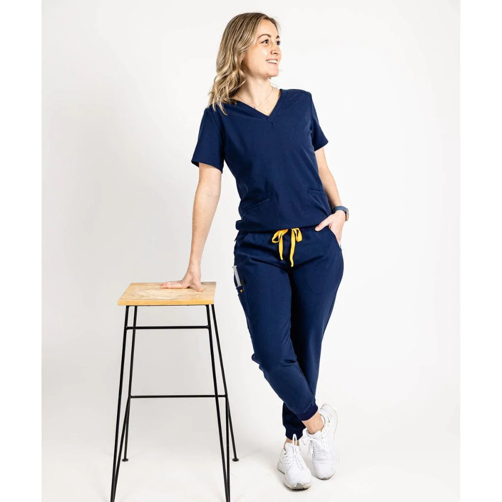 Full body leaning picture of the the Caswell scrub top in navy blue.