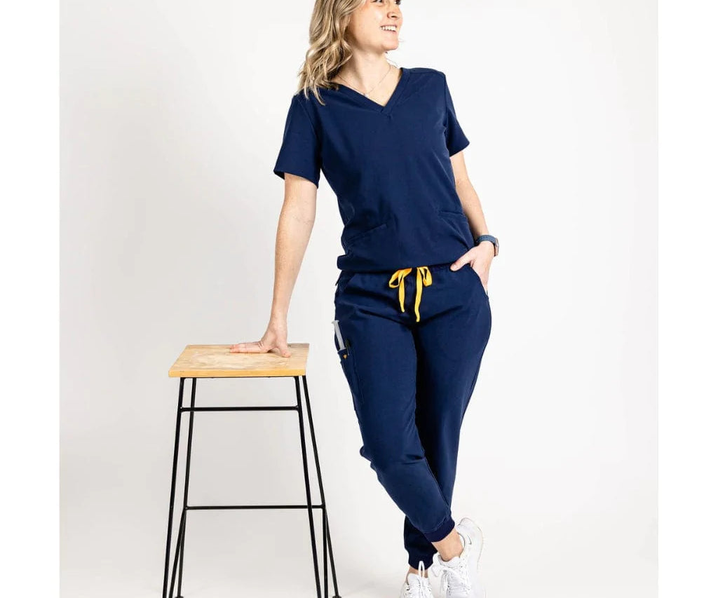 Full body leaning picture of the the Caswell scrub top in navy blue.